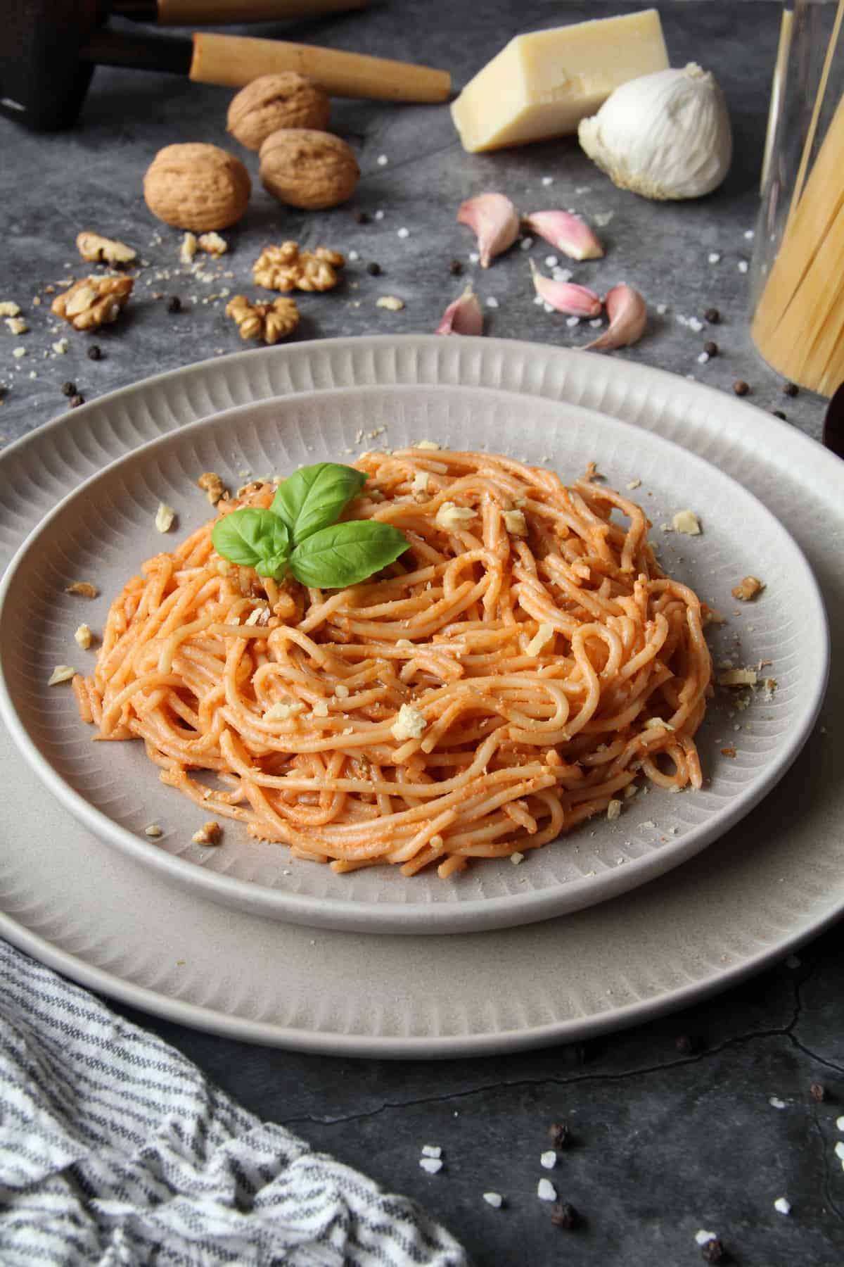 Ein Teller mit Spaghetti mit Walnuss-Pesto. Aussen herum Walnüsse, Knoblauch und Spaghetti als Deko.