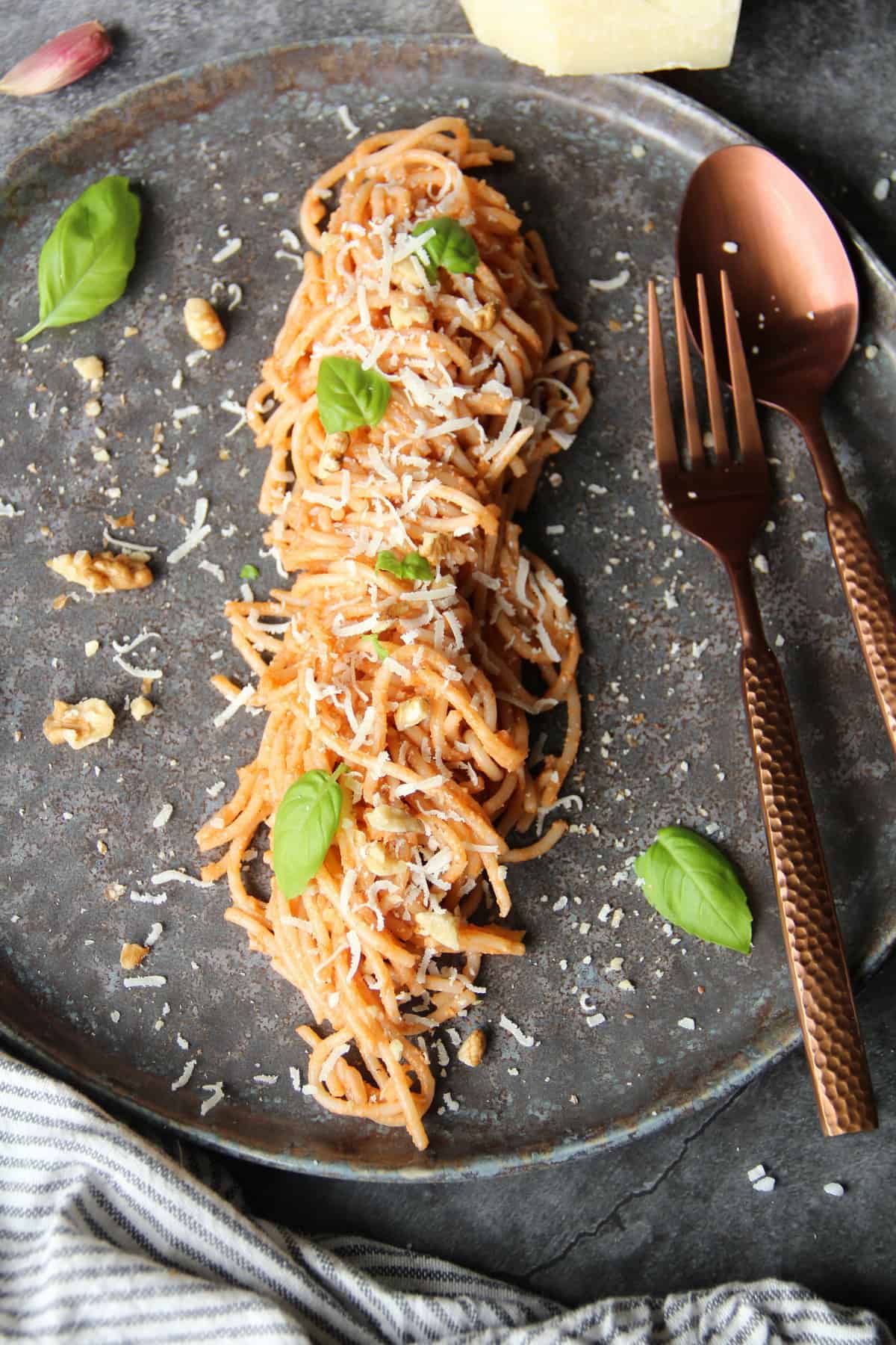 Ein dunkler Teller mit Spaghetti mit Walnuss-Pesto und Besteck.