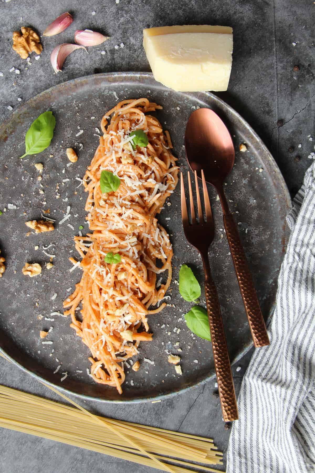 Ein dunkler Teller mit Spaghetti mit Walnuss-Pesto und Besteck.