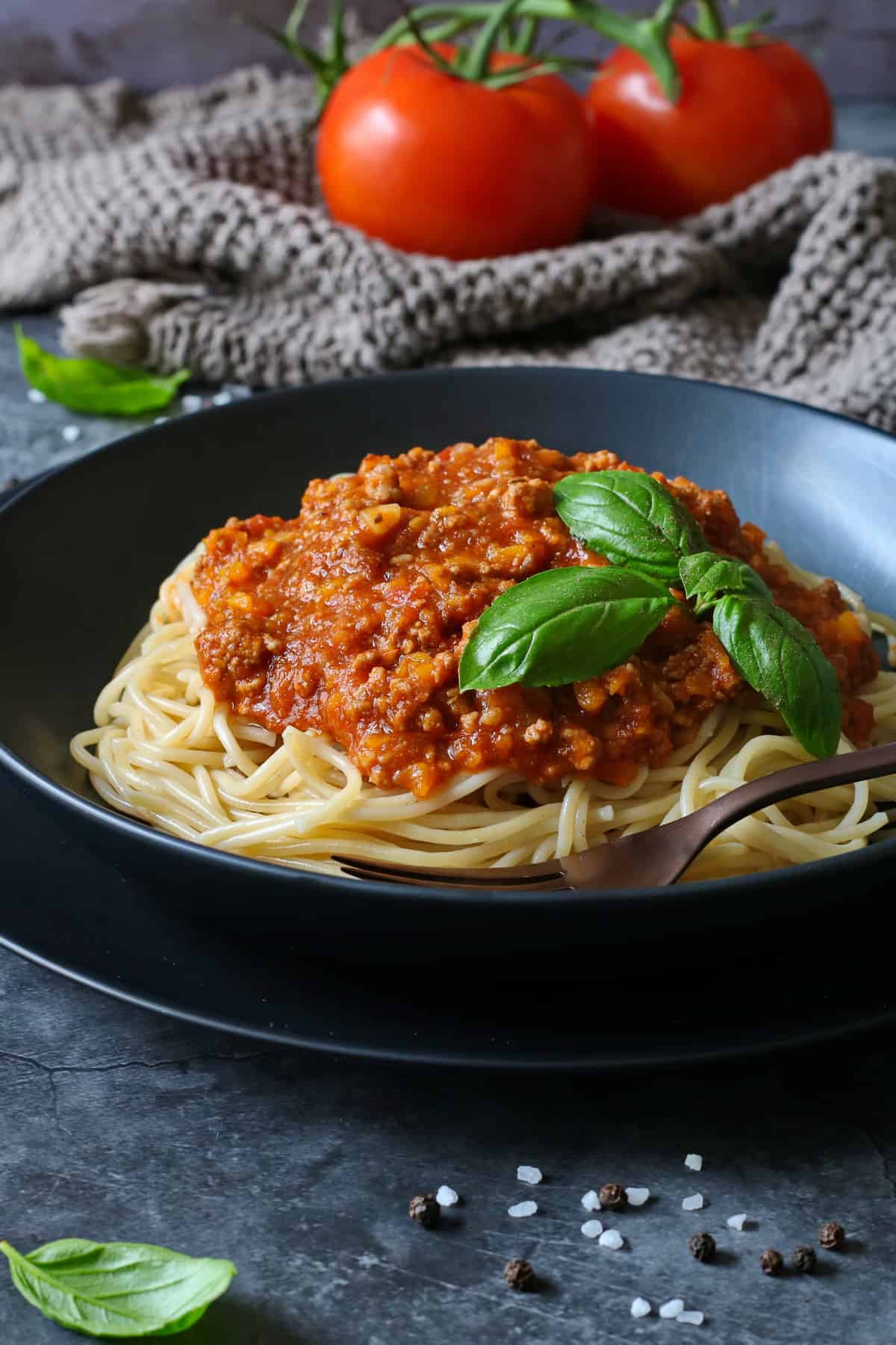 Ein schwarzer, tiefer Teller mit Spaghetti Bolognese.