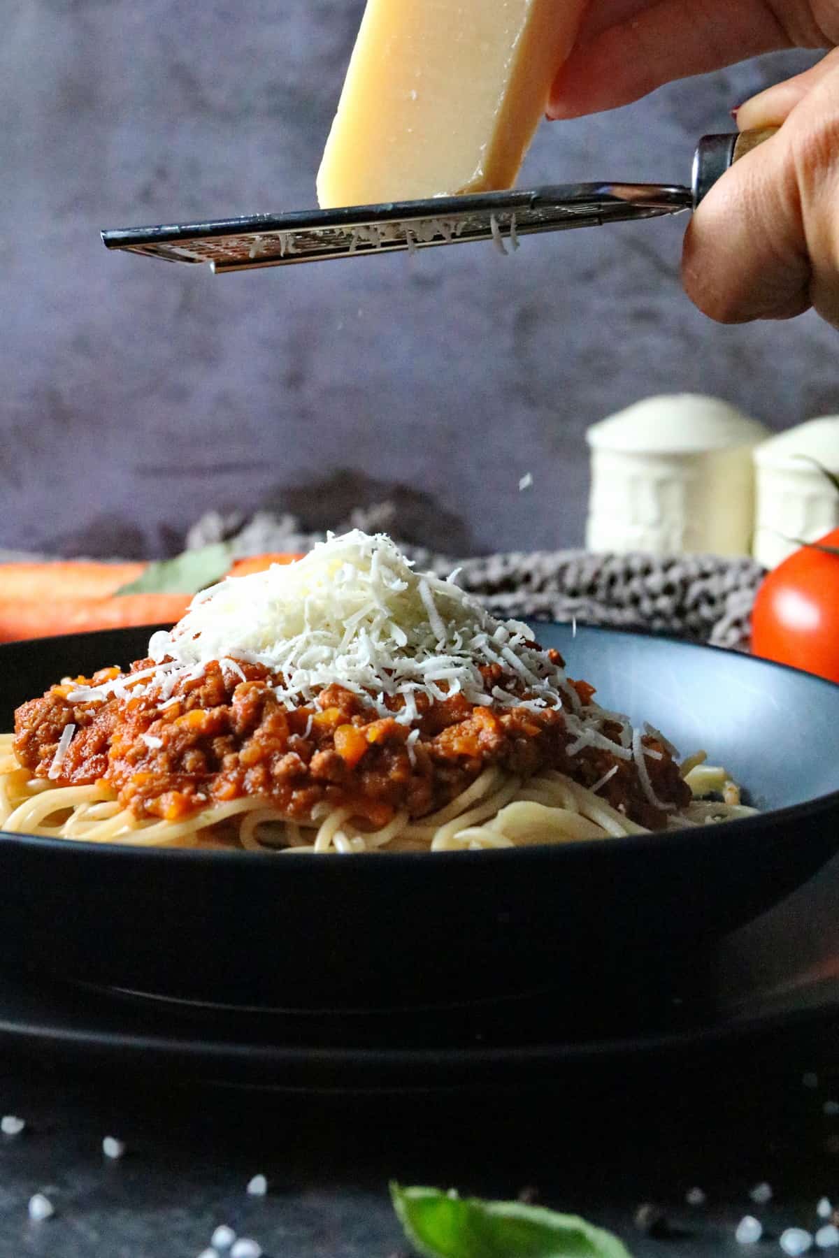 Parmesan wird über einen Teller mit Spaghetti Bolognese gerieben.