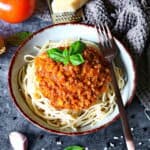 Ein tiefer Teller mit Spaghetti Bolognese und einer Gabel. Aussen herum Parmesan, Tomaten und Karotten als Deko.