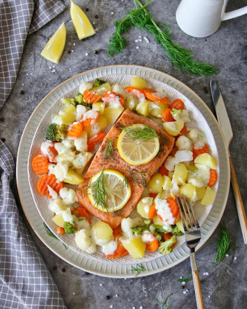 Ein Teller mit Lachsfilet mit Gemüse, Kartoffeln und Dillsoße.