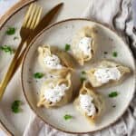 Ein Teller mit 5 Manti. Daneben goldfarbenes Besteck.