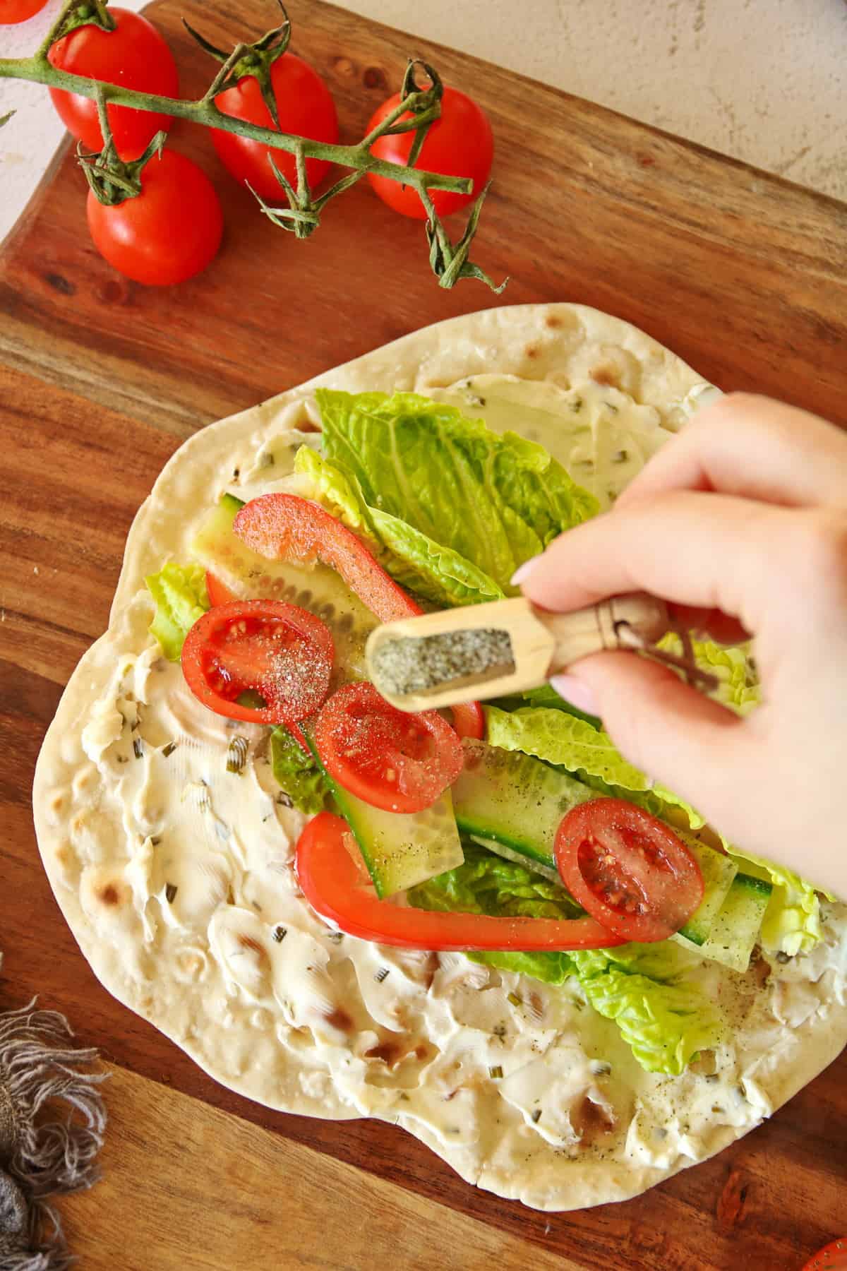 Eine Hand streut Gewürze auf einen ausgeklappten Wrap auf dem Salat und Gemüse leigt.