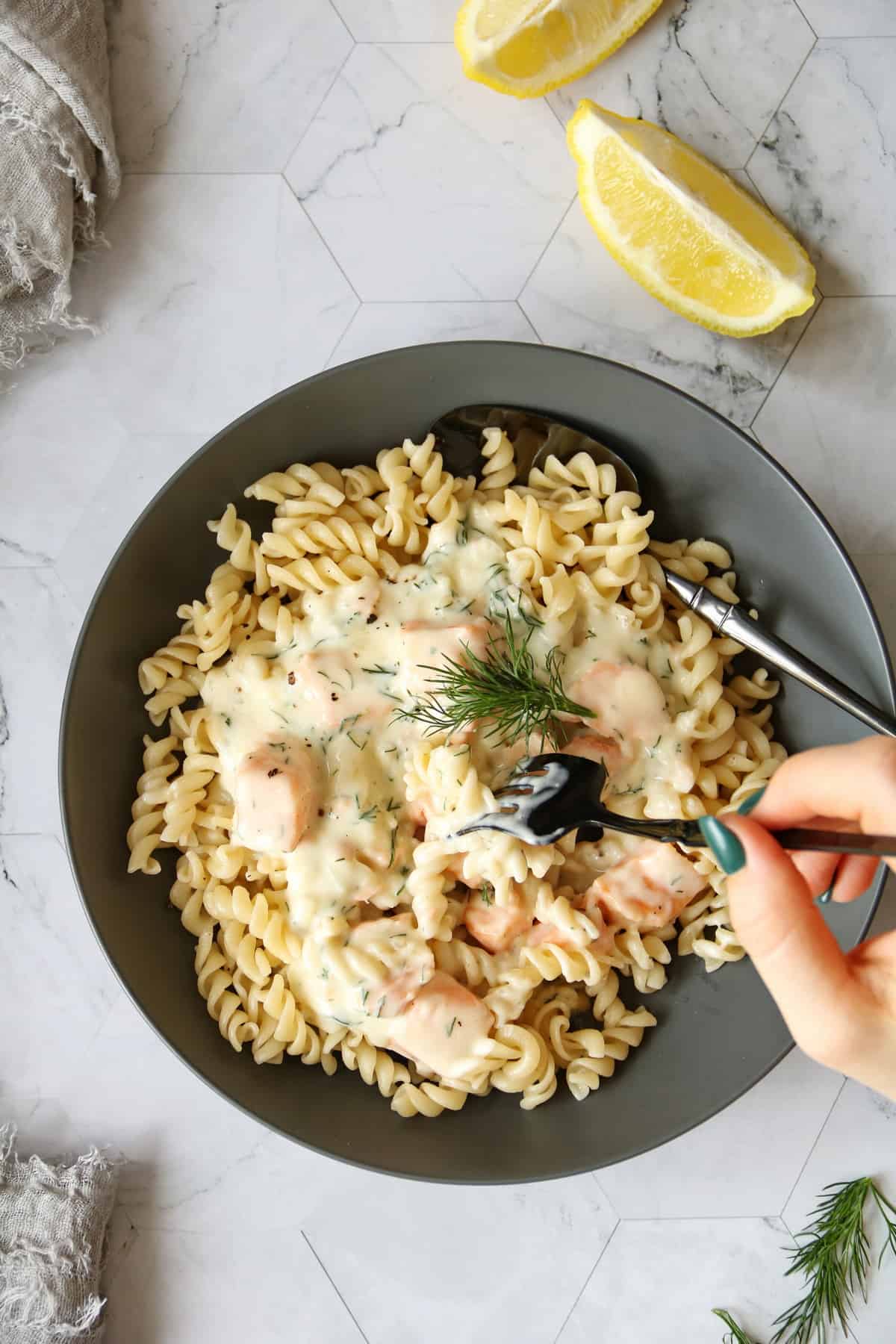 A hand takes a portion of pasta in salmon cream sauce from a plate with the dish.