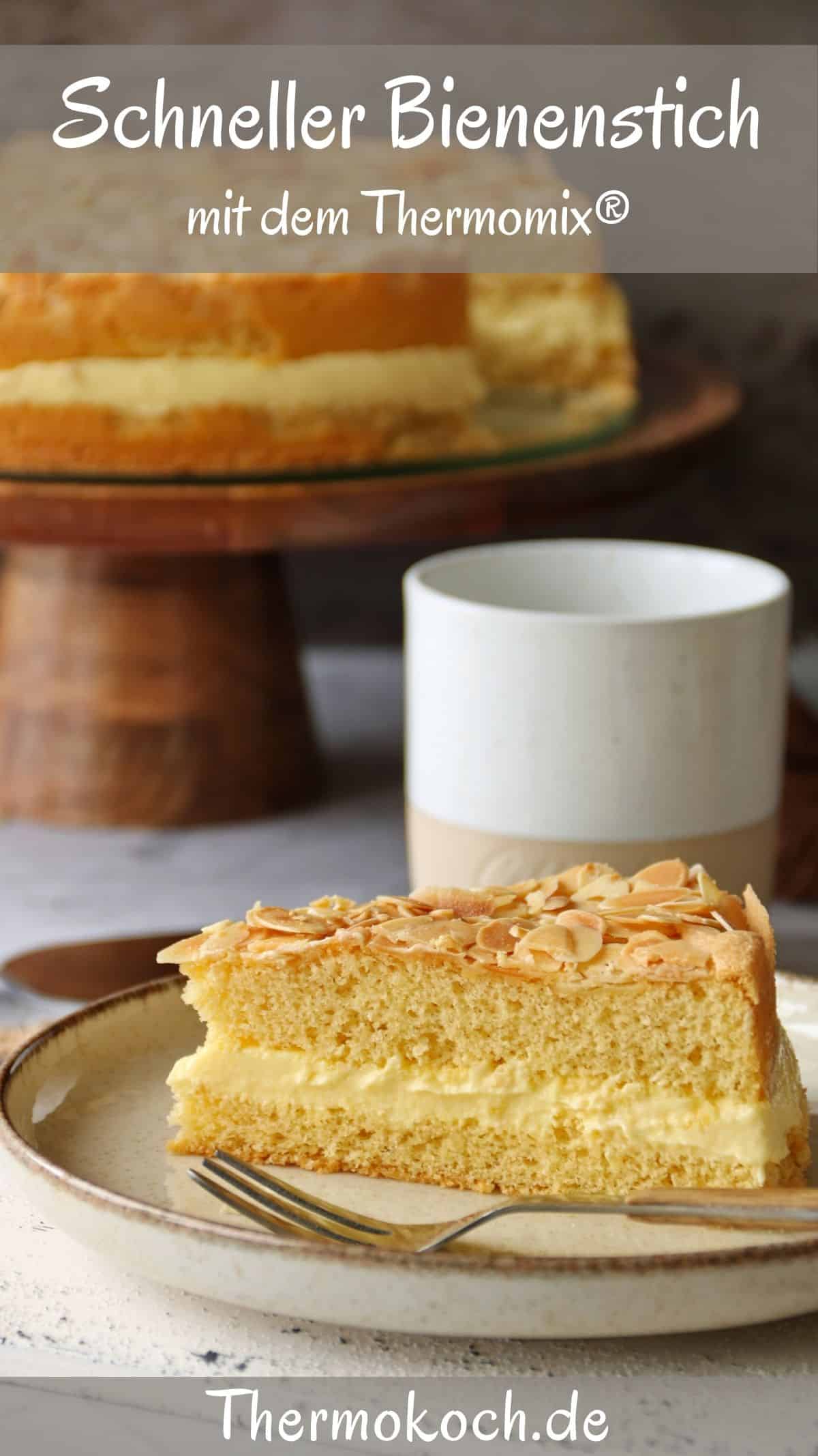 Ein Stück Bienenstich auf einem Teller. Im Hintergrund der übrige Kuchen auf einem Kuchenständer.
