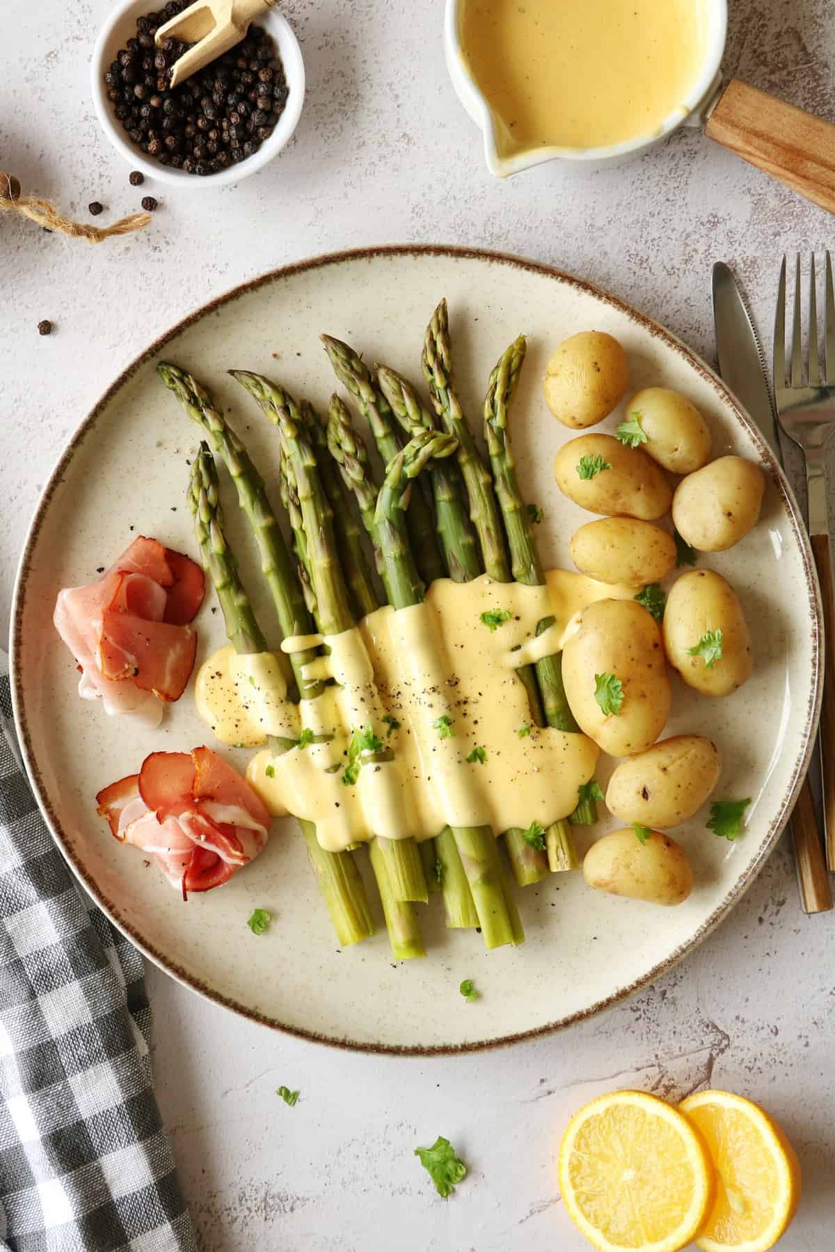 A plate of green asparagus with hollandaise sauce, potatoes and ham.