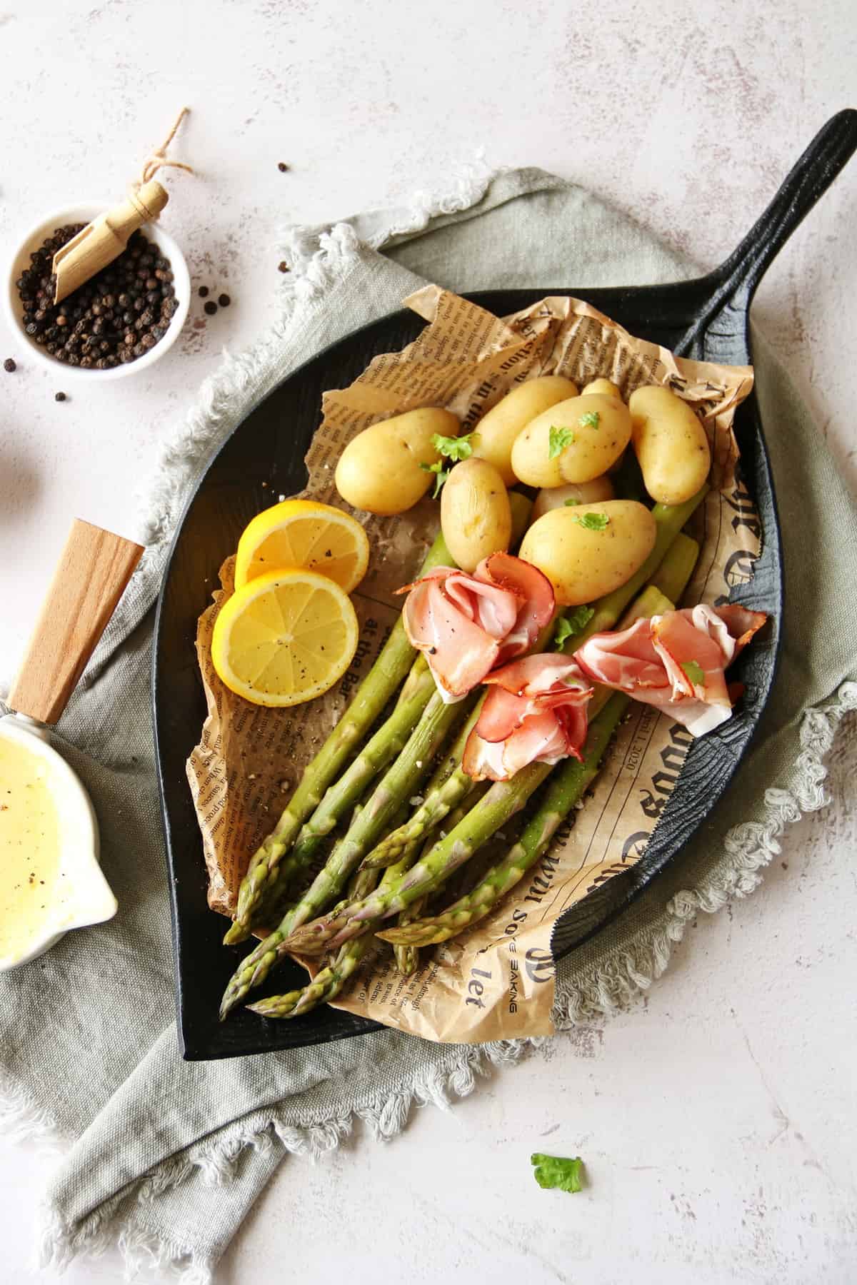 A bowl of green asparagus with hollandaise sauce, potatoes and ham.