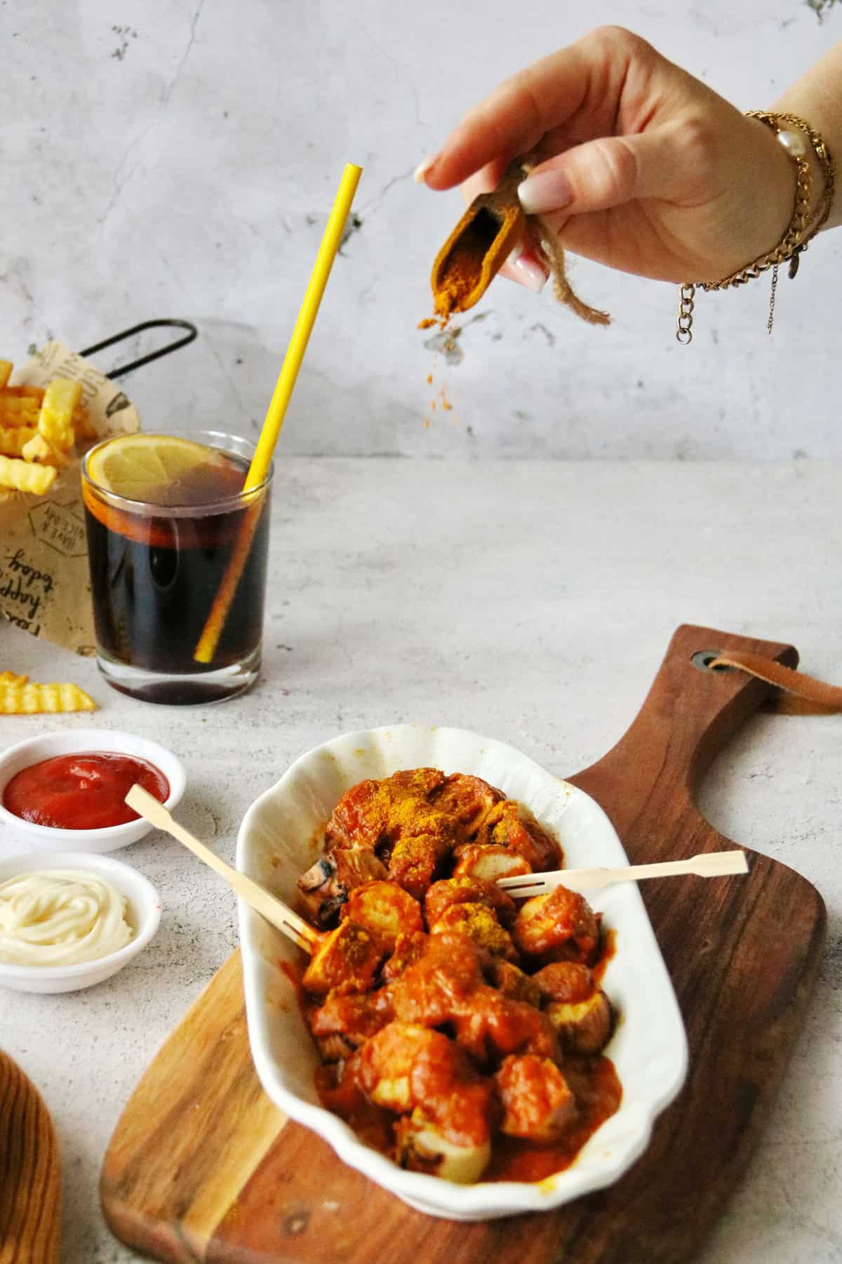 Eine Hand streut Currypulver auf eine Schale mit Currywurst und Currysoße.