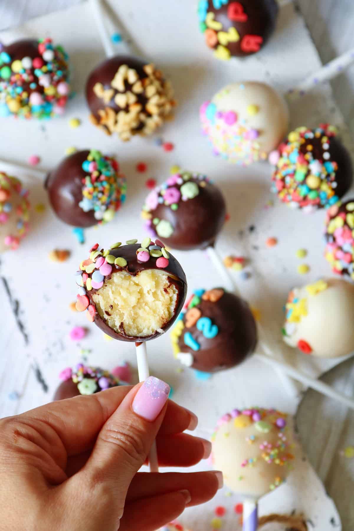 Eine Hand hält einen angebissenen Cake Pop. Im Hintergrund mehrere Cake Pops.