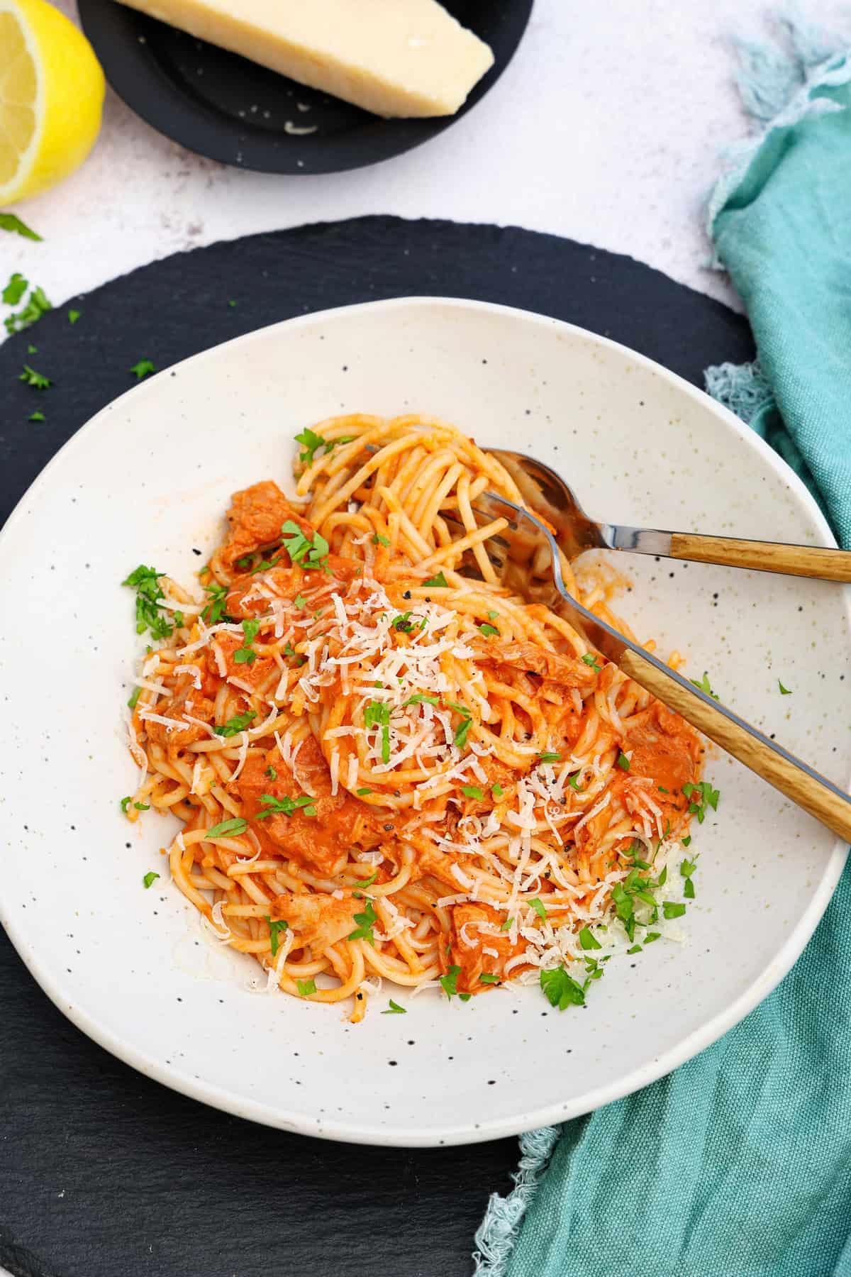 A white plate of spaghetti with tuna and tomato sauce.