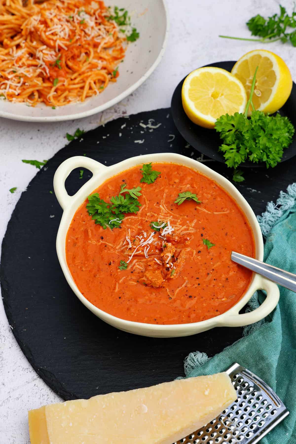 Eine Schale mit Thunfisch-Tomatensoße. Im Hintergrund ein weißer Teller mit Spaghetti mit Thunfisch-Tomatensoße.