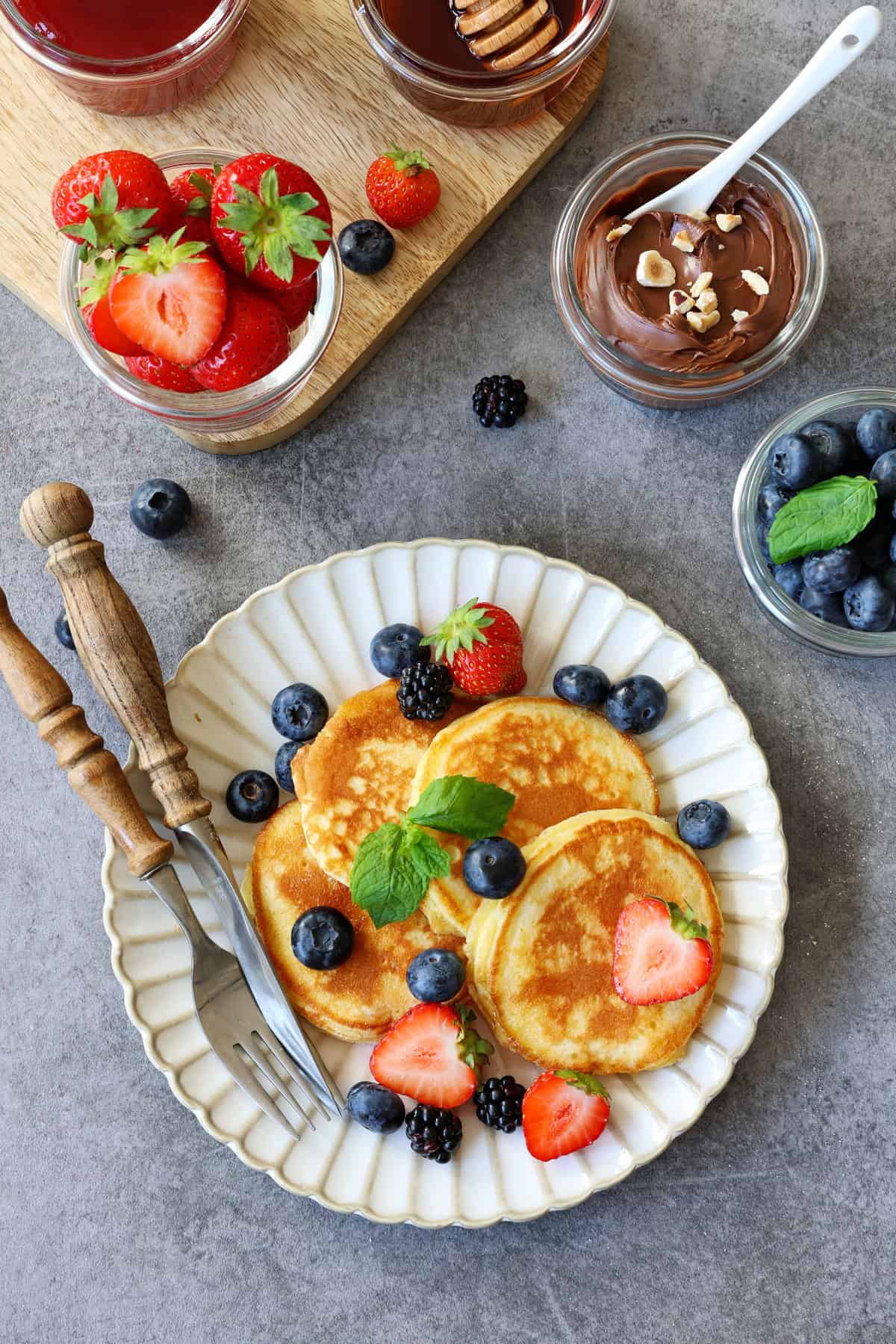 Pancakes und Beeren auf einem Teller. Darüber Beeren und Aufstrich als Deko.