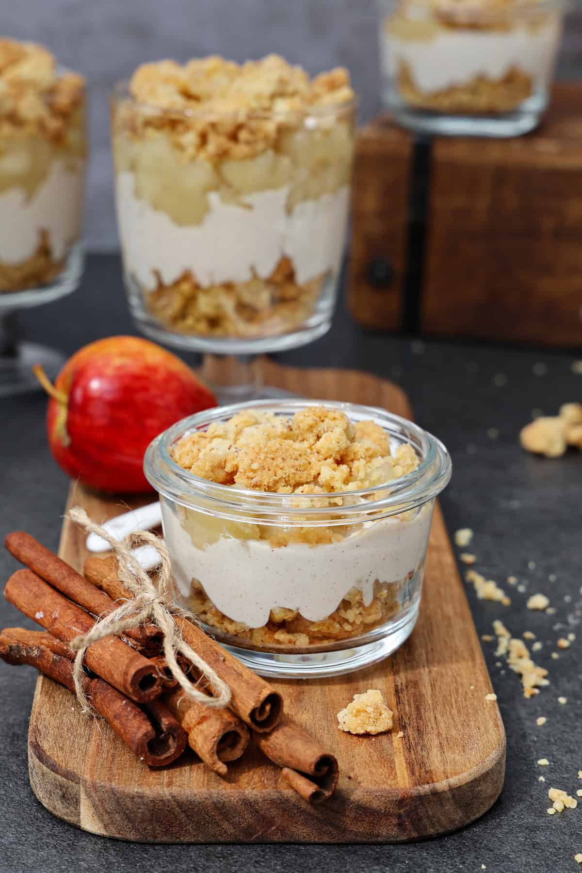 Mehrere dekorativ angerichtete Gläser mit Apfel-Quark-Dessert mit Streuseln.