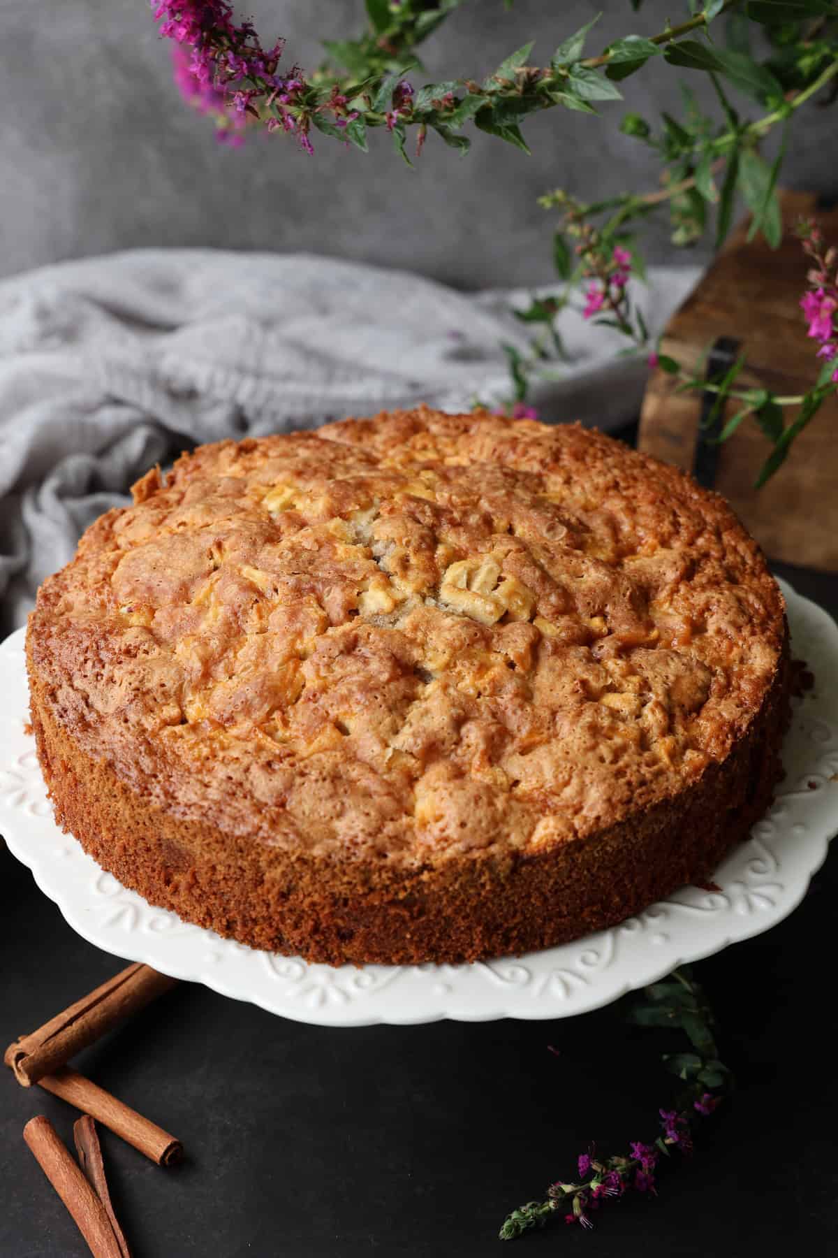 Ein Apfel-Walnusskuchen mit Zimt auf einem runden weißen Kuchenständer.