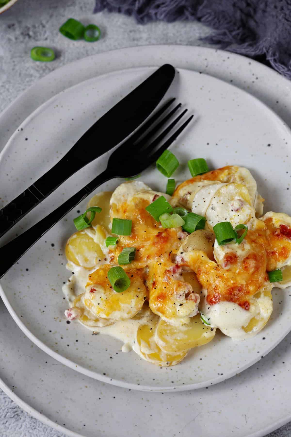 Ein Teller mit einer Portion Kartoffelgratin und Besteck.