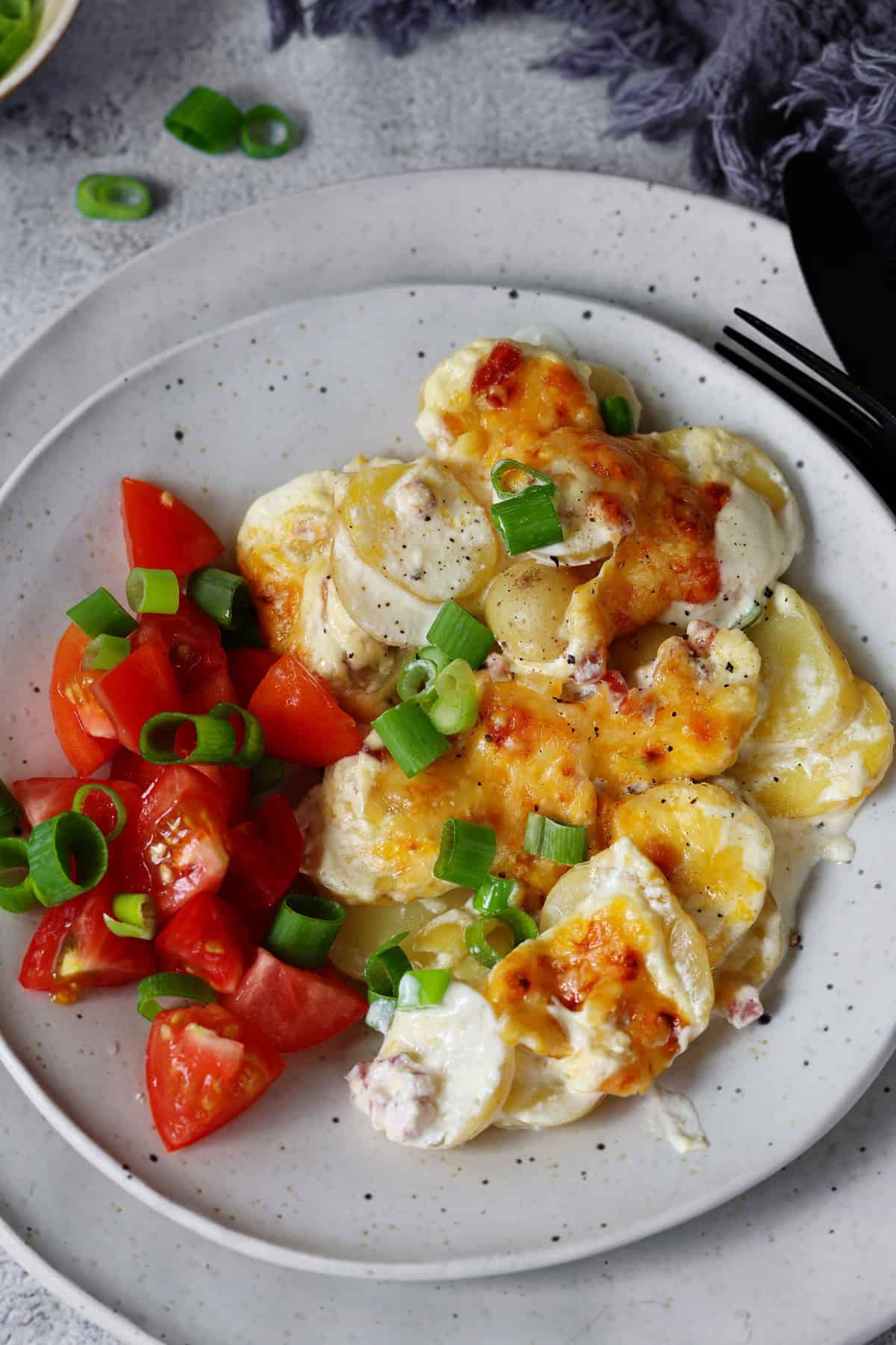 Ein Teller mit einer Portion Kartoffelgratin und einem Tomatensalat.