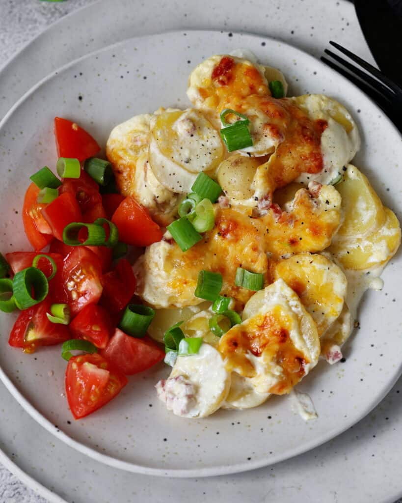 Ein Teller mit einer Portion Kartoffelgratin und einem Tomatensalat.