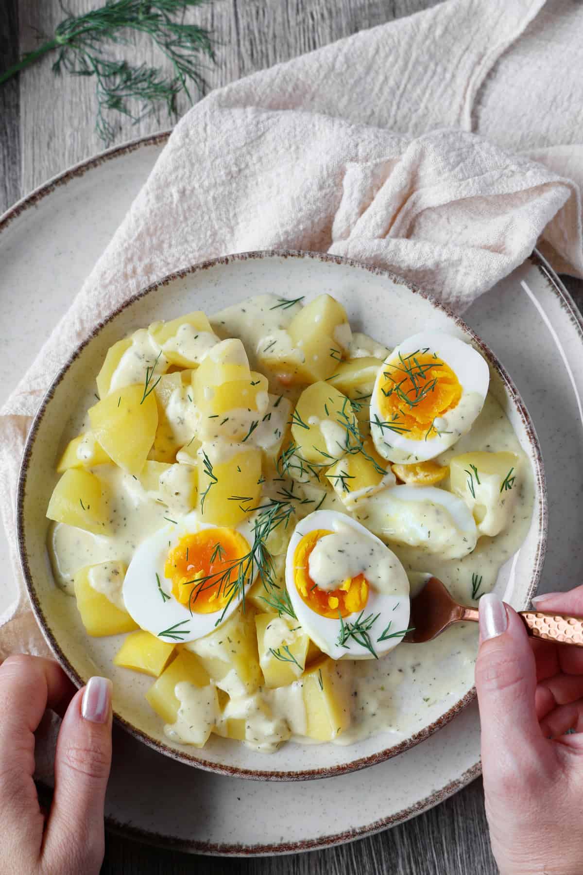 Ein Teller mit Eiern in Senfsoße und Kartoffeln, von dem eine Portion mit einer Gabel genommen wird.