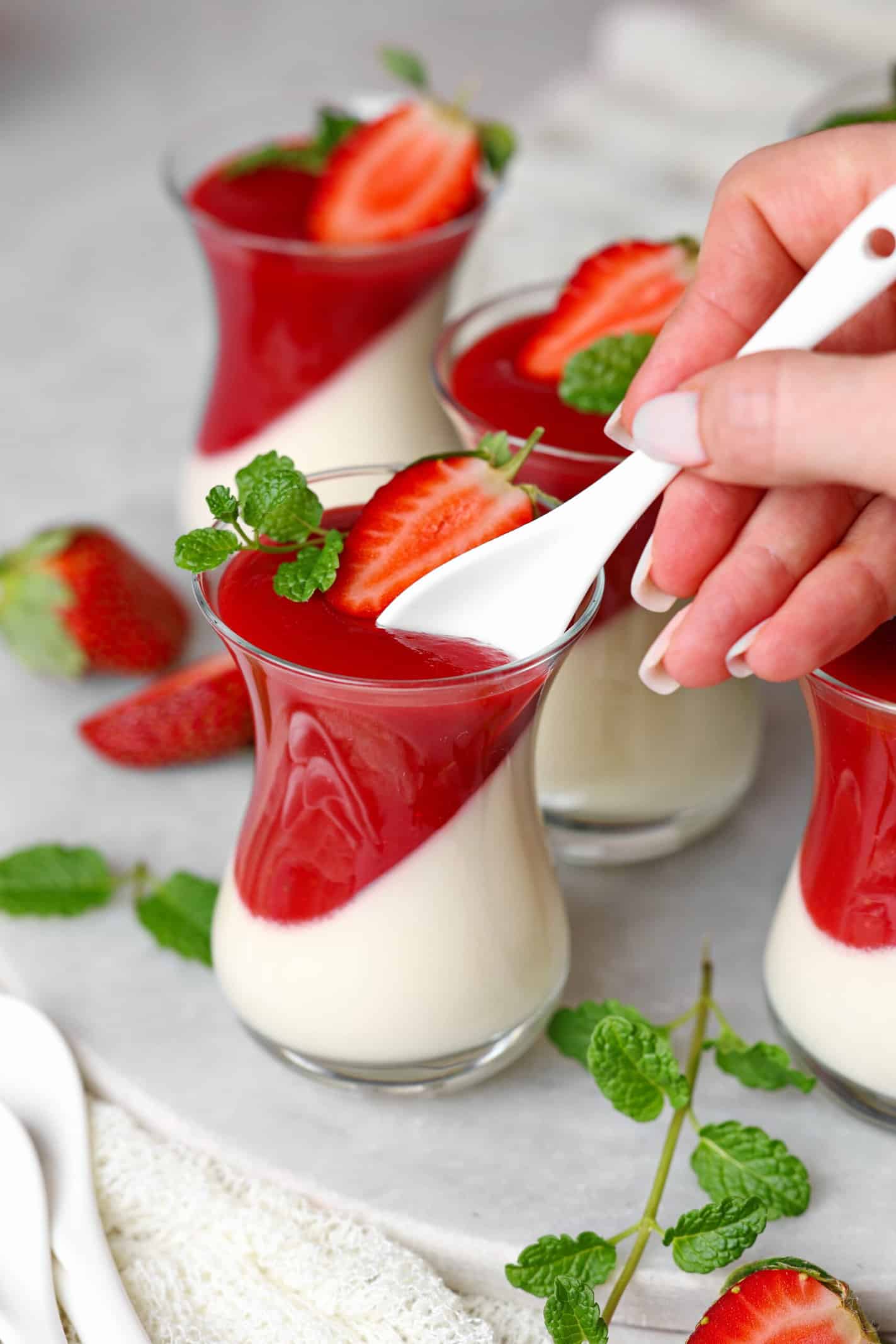 Mehrere Gläser Panna cotta mit Erdbeersoße.