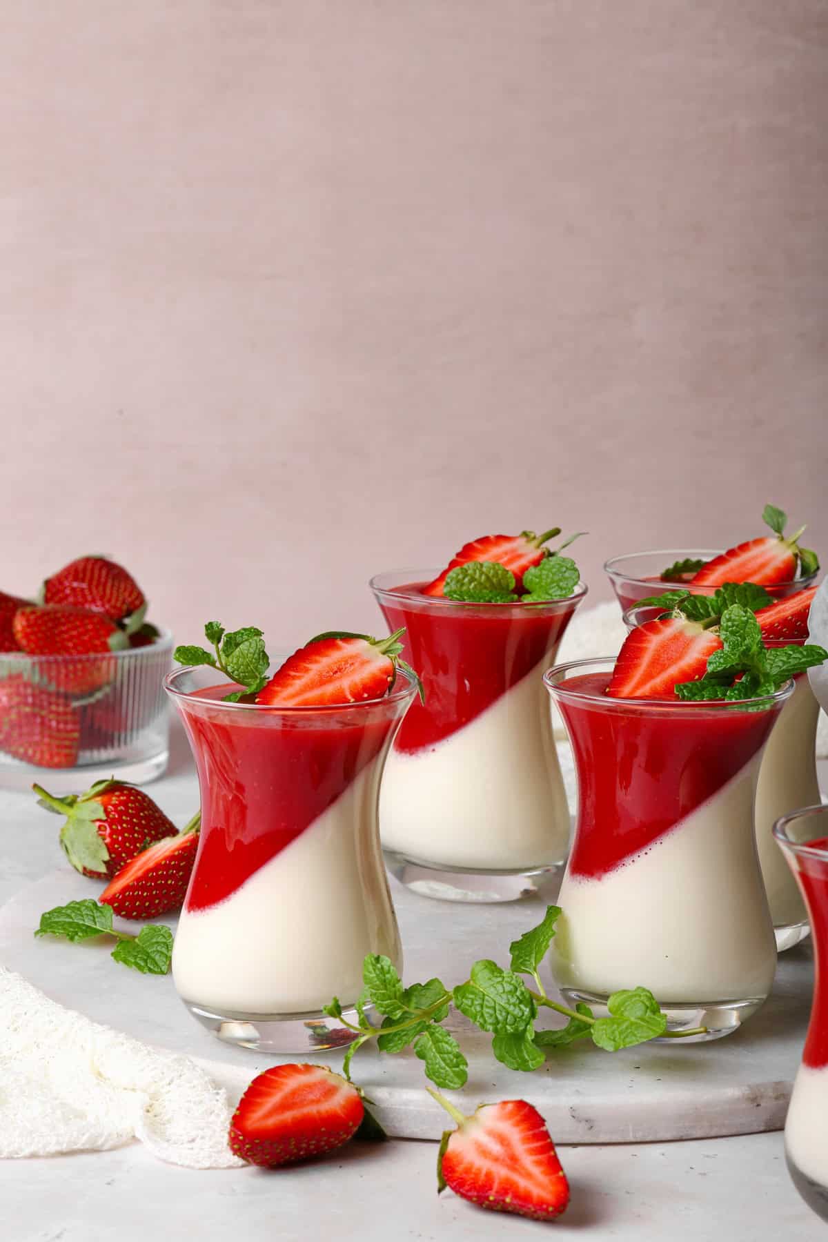 Mehrere Gläser Panna cotta mit Erdbeersoße.