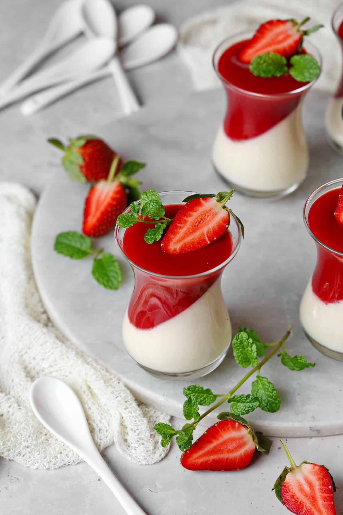 Mehrere Gläser Panna cotta mit Erdbeersoße.