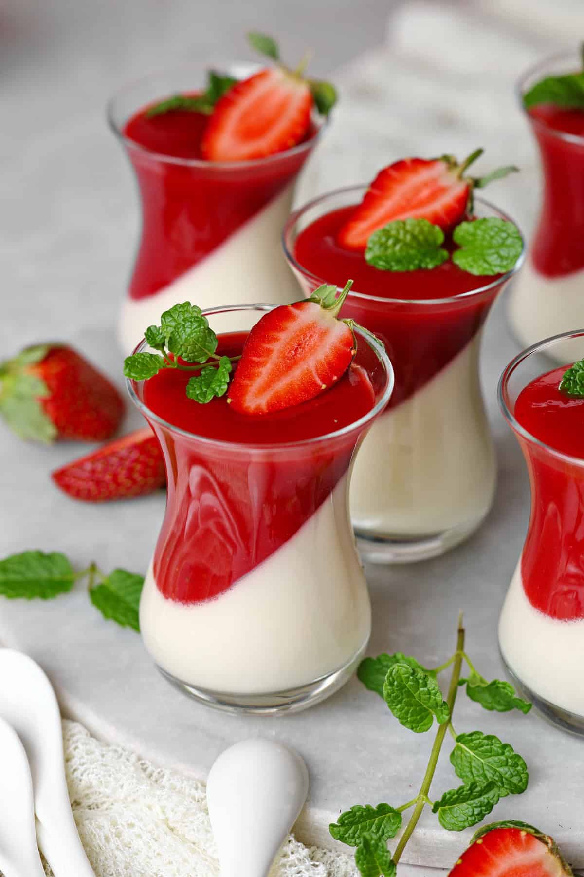 Mehrere Gläser Panna cotta mit Erdbeersoße.