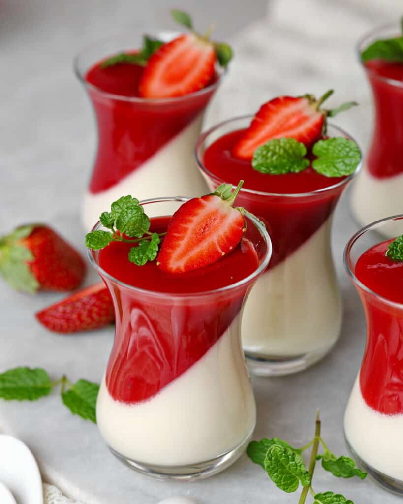 Mehrere Gläschen Panna cotta mit Erdbeersoße.