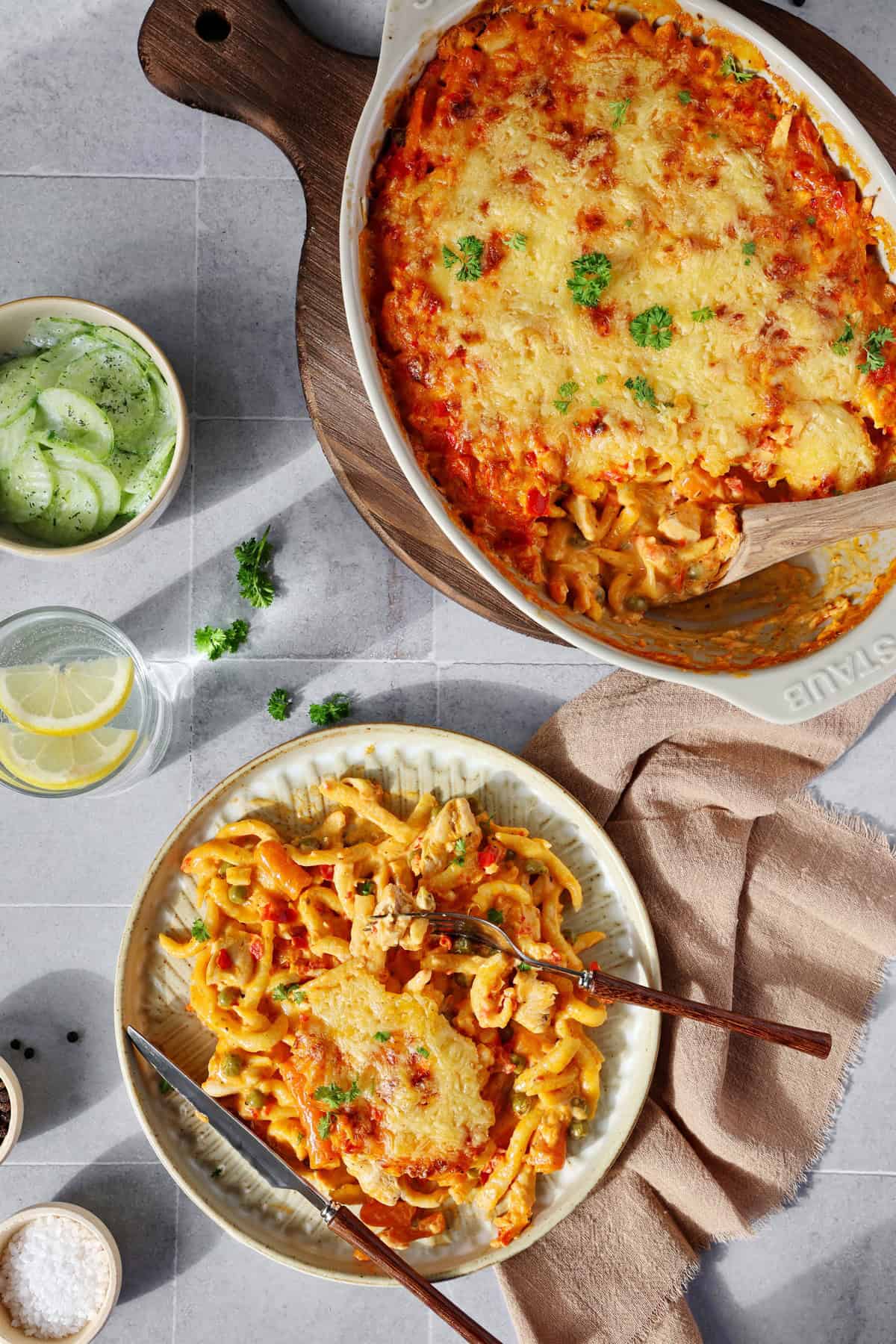 Ein Teller mit Spätzle-Auflauf und darüber eine Auflaufform mit Spätzle-Auflauf mit Hähnchen.