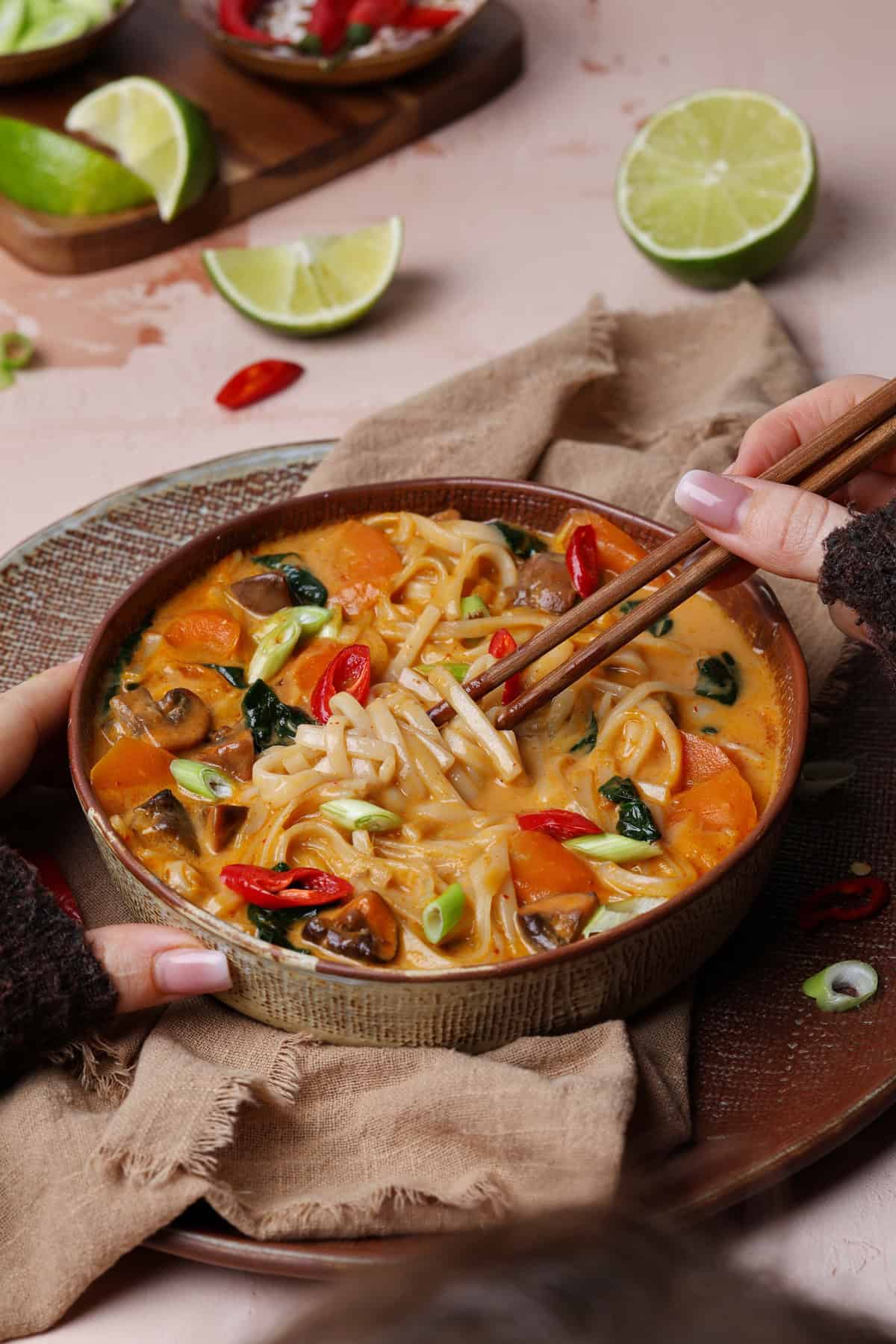 Zwei Hände mit Essstäbchen halten eine Suppenschale mit Thai-Kokos-Suppe.