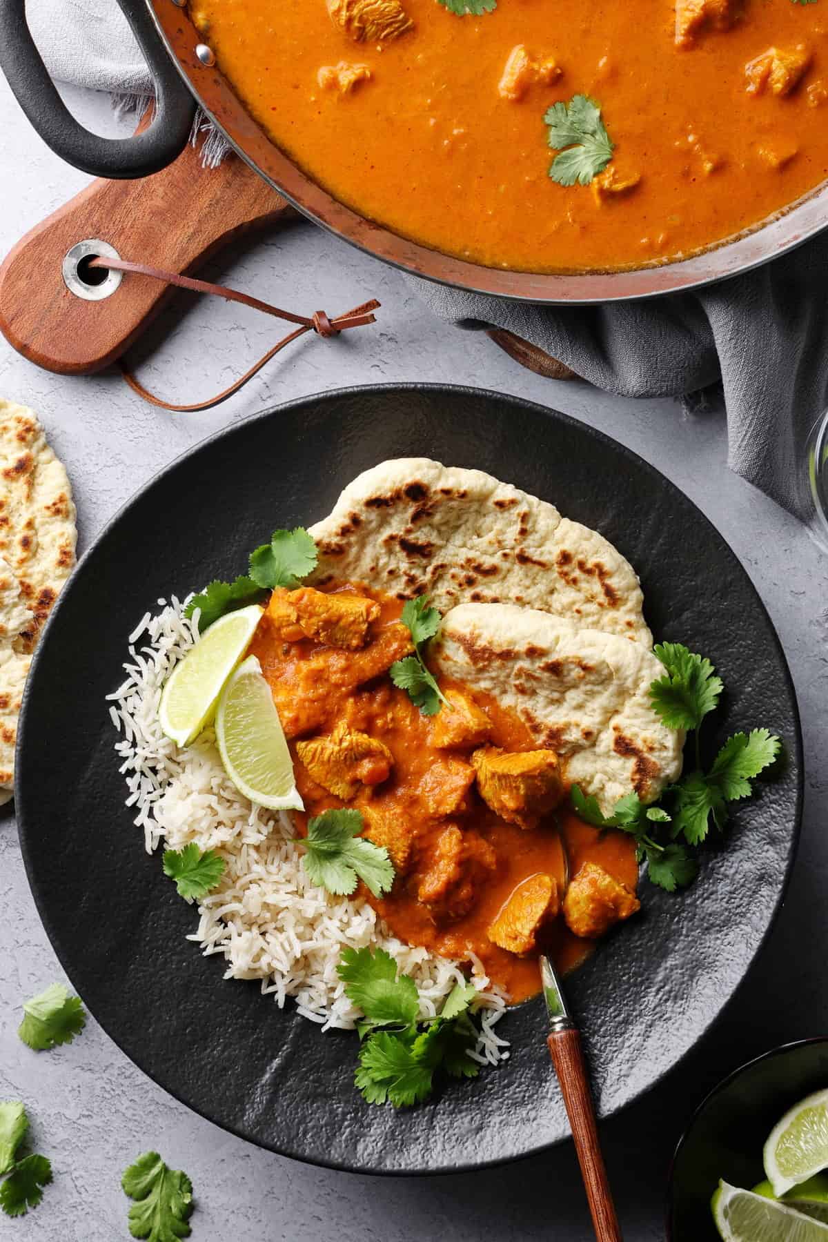 Ein dunkler Teller mit Butter Chicken, Reis und Naan Brot.