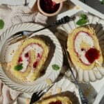 Mehrere Stücke Preiselbeeren-Mascarpone-Biskuitrolle auf Kuchentellern.
