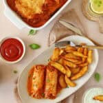 Eine weiße Auflaufform mit Schinken-Hack-Röllchen und ein Teller mit Schinken-Hack-Röllchen und Pommes.