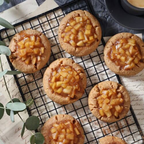 Frisch gebackene Apfel-Zimt-Cookies mit gewürfelter Apfelfüllung liegen auf einem schwarzen Kuchengitter.