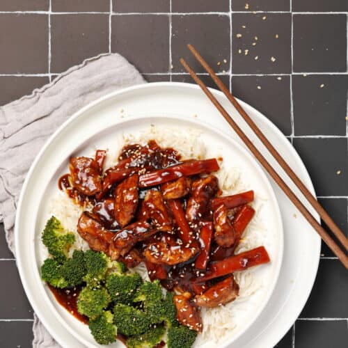 Ein weißer Teller mit asiatischem Hähnchen mit Gemüse und Reis.