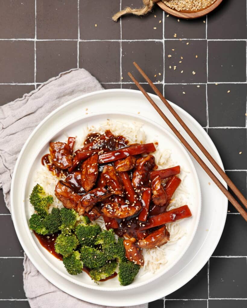 Ein weißer Teller mit asiatischem Hähnchen mit Gemüse und Reis.