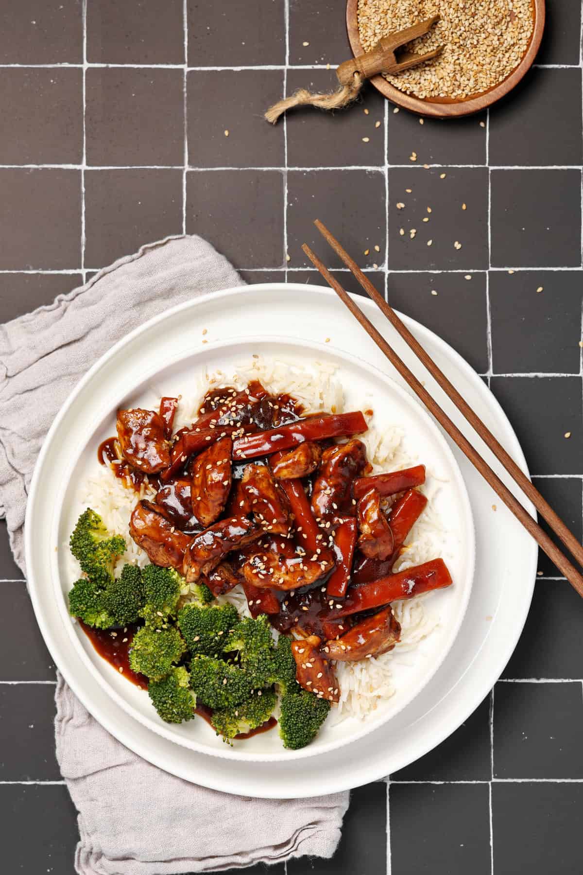 Ein weißer Teller mit asiatischem Hähnchen mit Gemüse und Reis.
