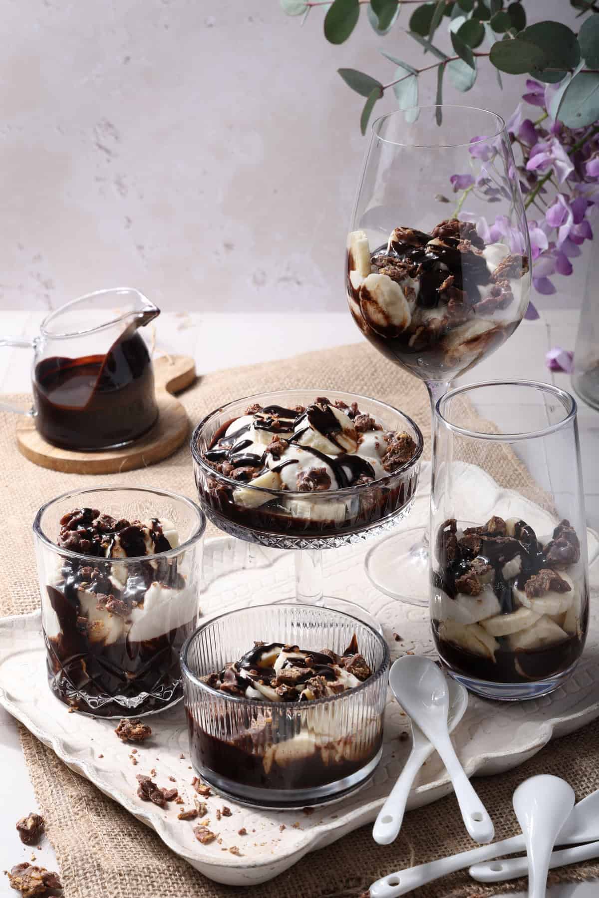 A hand holding an individual glass filled with banana split dessert.