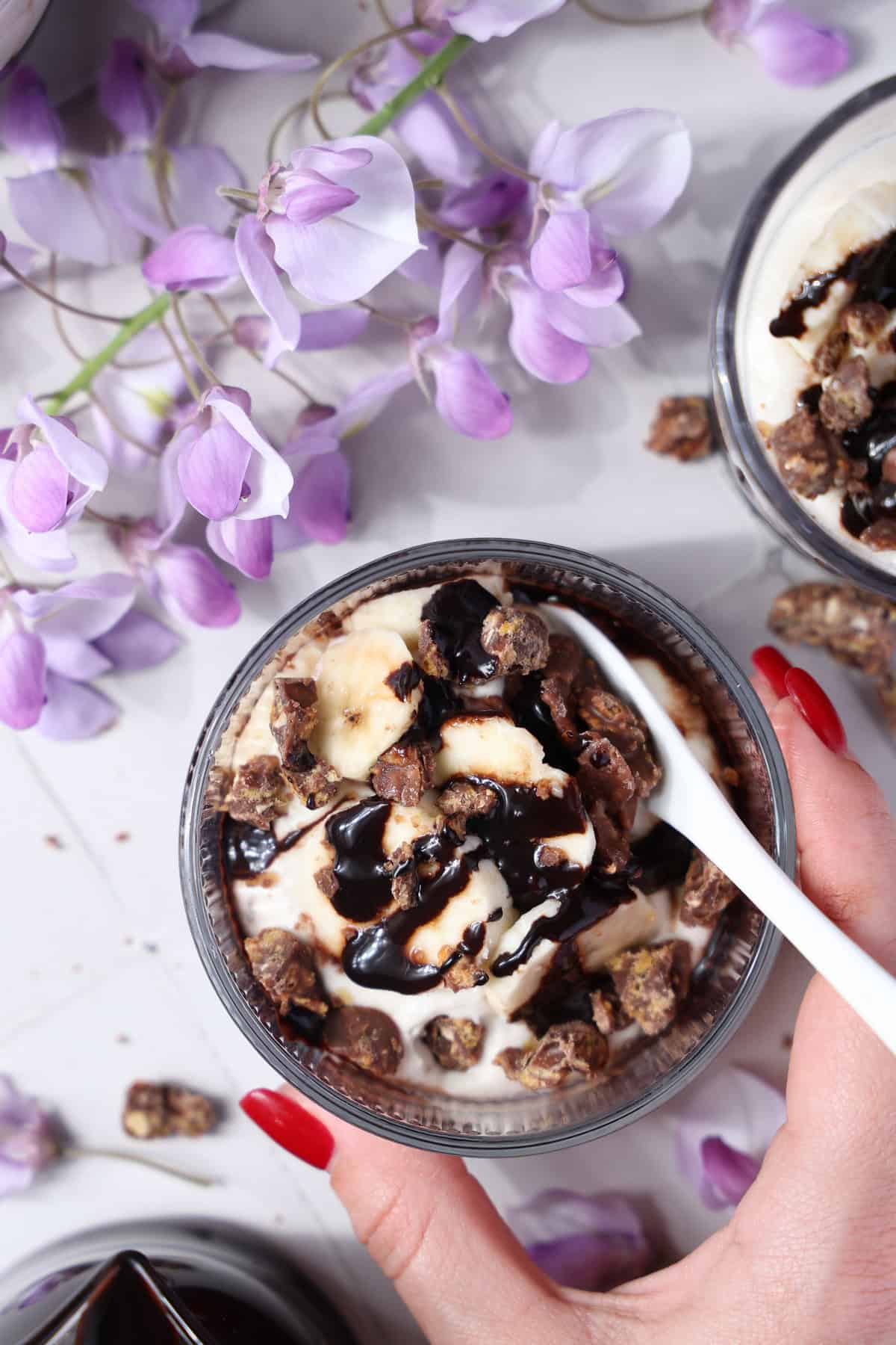 A hand holding a glass of banana split dessert.