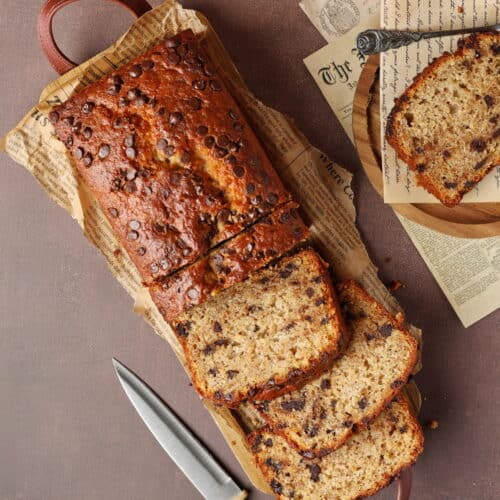 Ein saftiges, in Scheiben geschnittenes Bananenbrot mit Schokodrops liegt auf einem hölzernen Servierbrett.