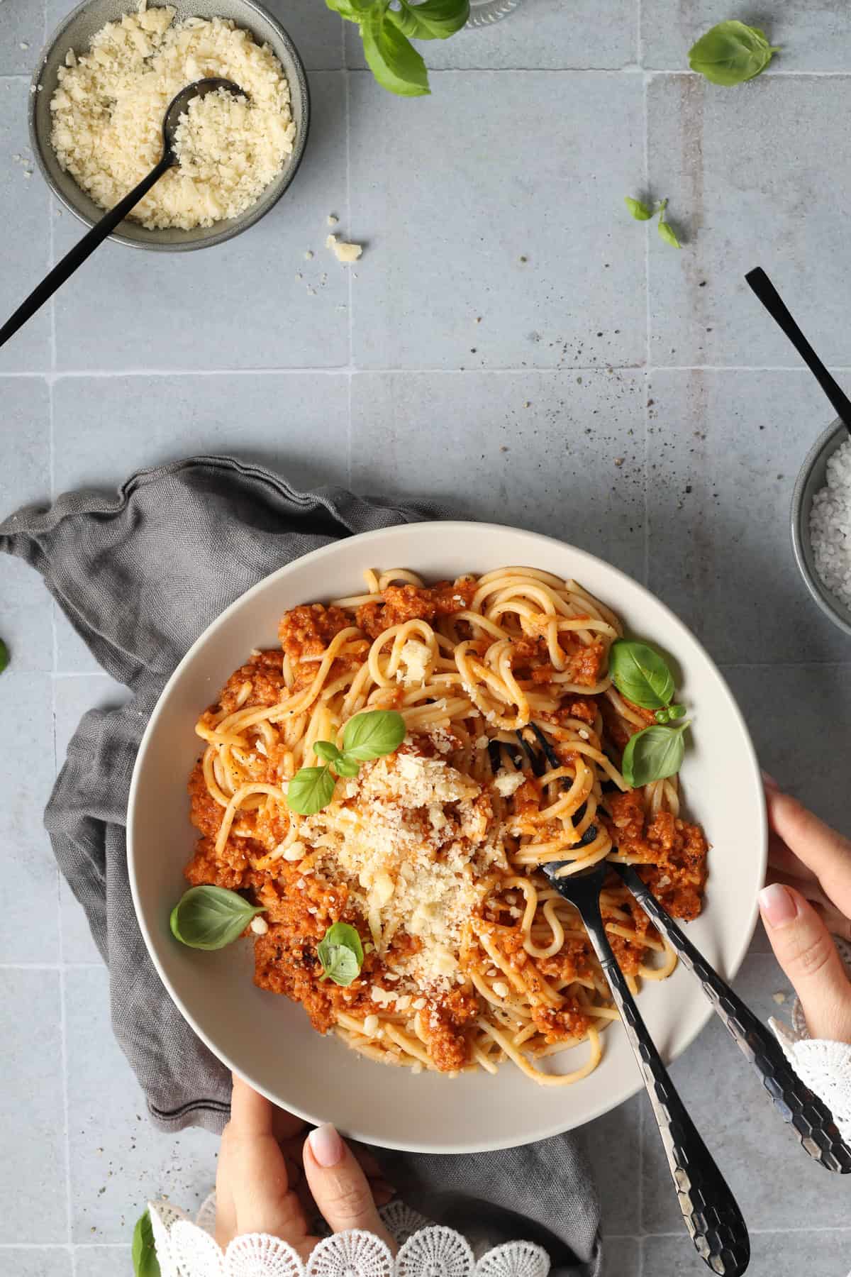 Two hands holding a deep white bowl filled with cauliflower mushroom Bolognese and spaghetti.
