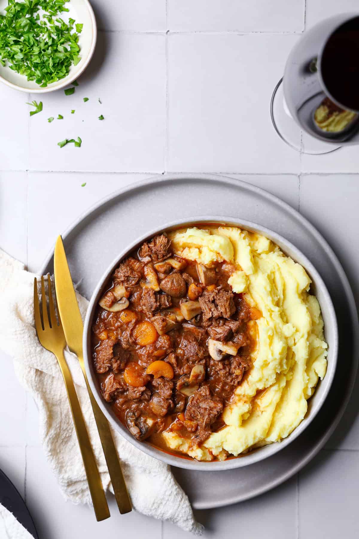 Ein Teller mit Boeuf Bourguignon und Kartoffelpüree. Links daneben goldenes Besteck.