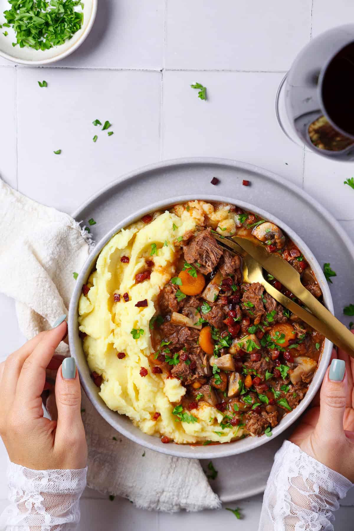 Two hands holding a plate of Boeuf Bourguignon served with mashed potatoes.