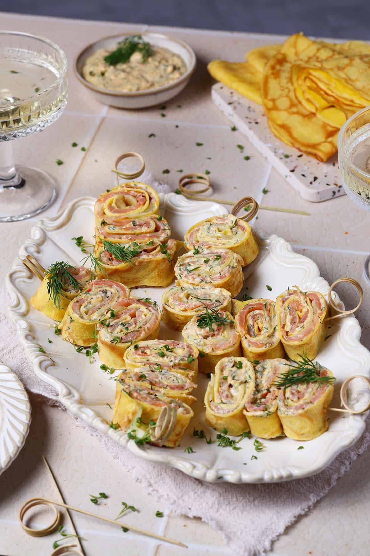 Crêpes-Röllchen mit Lachs und Frischkäse-Dill-Creme auf einer weißen Servierplatte.