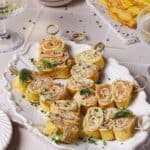 Crêpes-Röllchen mit Lachs und Frischkäse-Dill-Creme auf einer weißen Servierplatte.