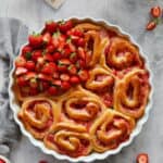 Eine runde Auflaufform mit Erdbeerschnecken und frischen Erdbeeren. Außen herum Erdbeeren als Deko.