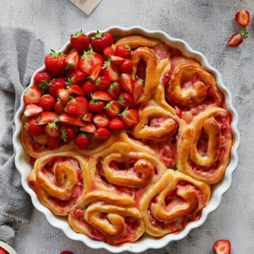 Eine runde Auflaufform mit Erdbeerschnecken und frischen Erdbeeren. Außen herum Erdbeeren als Deko.