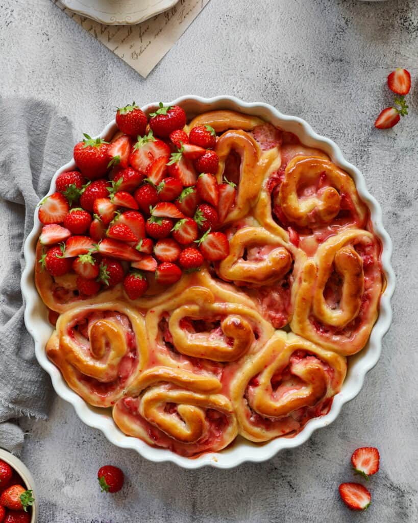 Eine runde Auflaufform mit Erdbeerschnecken und frischen Erdbeeren. Außen herum Erdbeeren als Deko.
