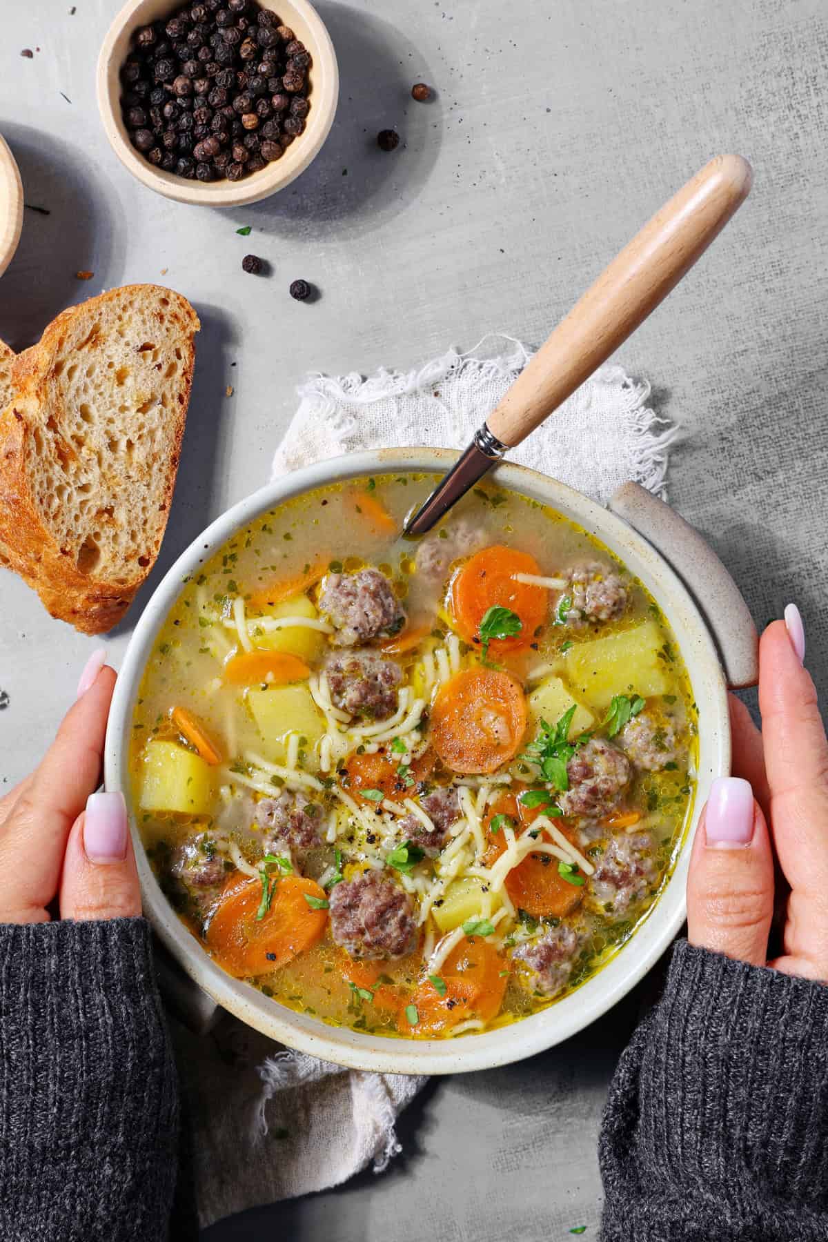 Two hands holding a white bowl of cozy meatball soup.